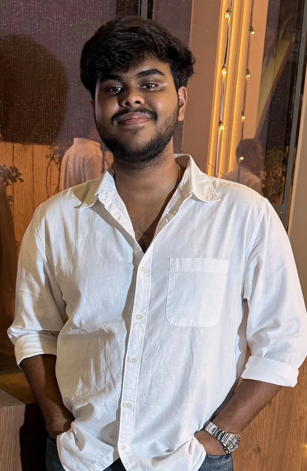 Portrait of Abilaash in a white shirt, standing beside a warmly lit window